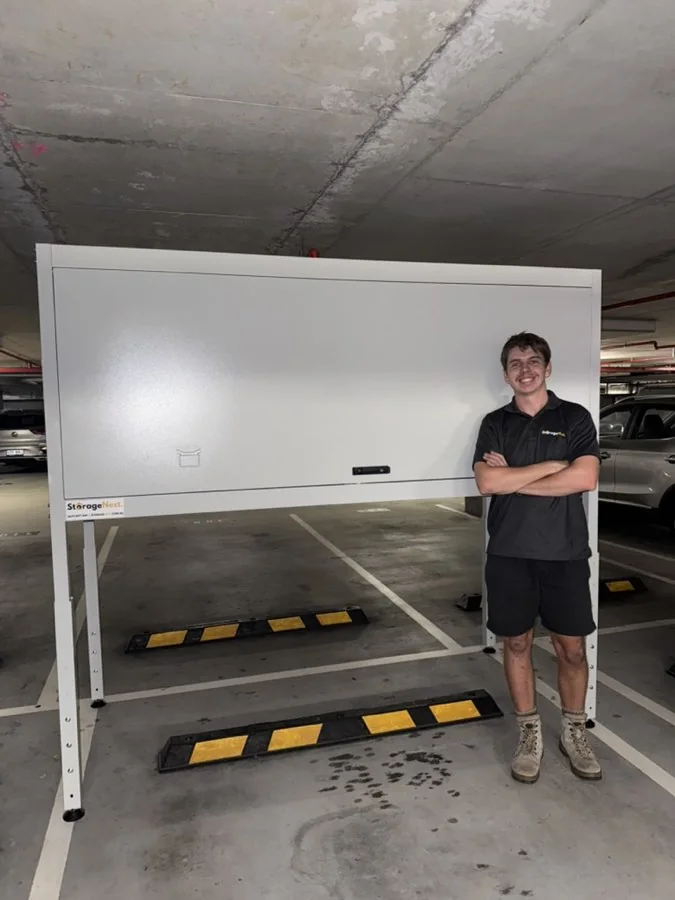 A StorageNest installer standing beside a newly installed Kookaburra over bonnet storage unit in an apartment car park